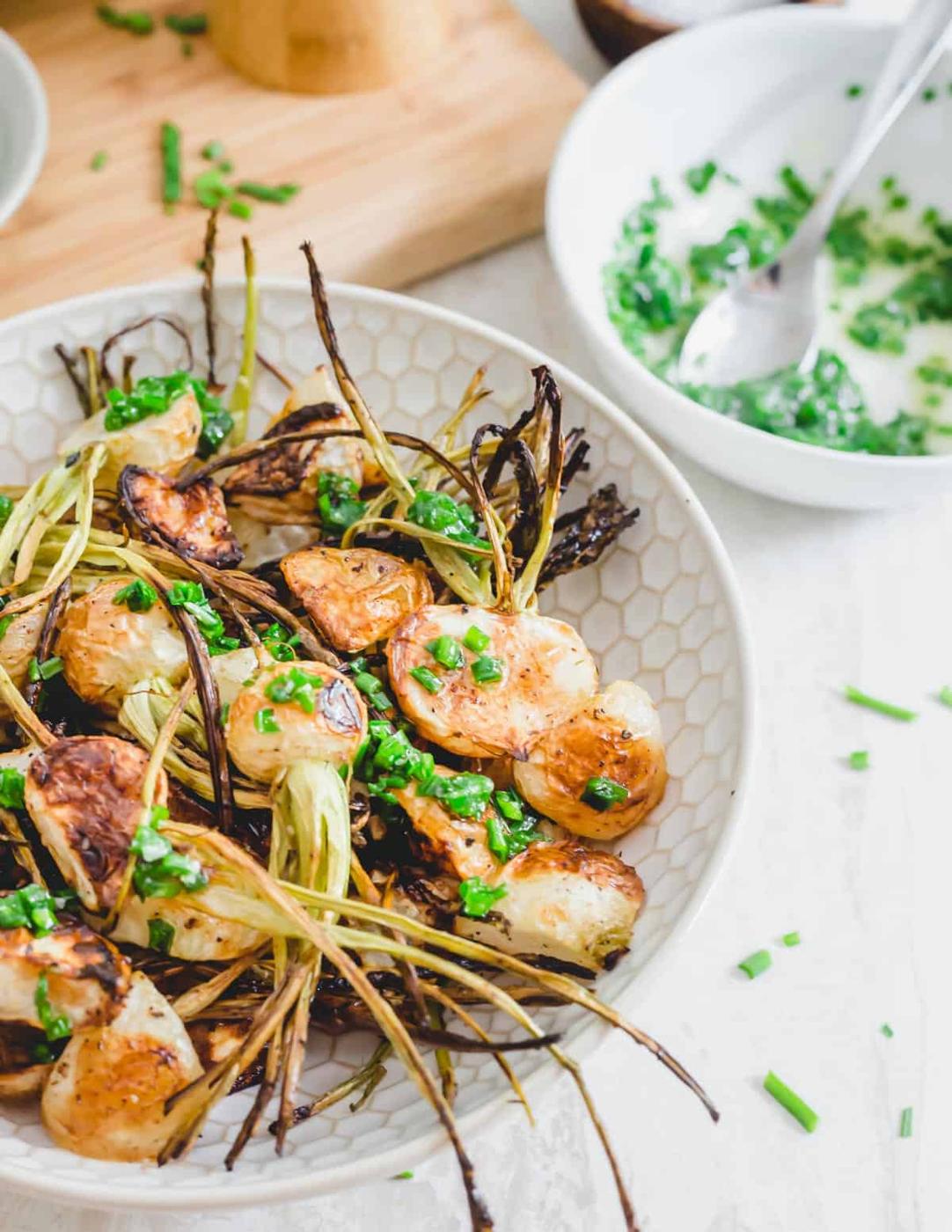 Crispy roasted turnips with stems attached in a bowl drizzled in a melted butter chive sauce.