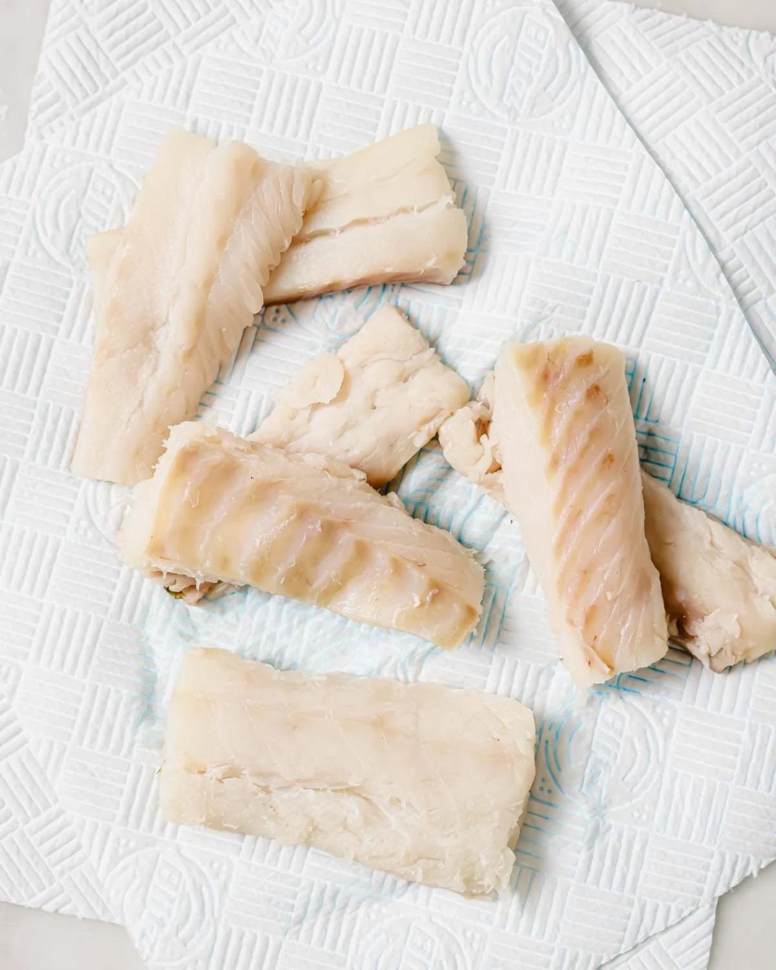 Pieces of raw cod, placed on a textured white paper towel.