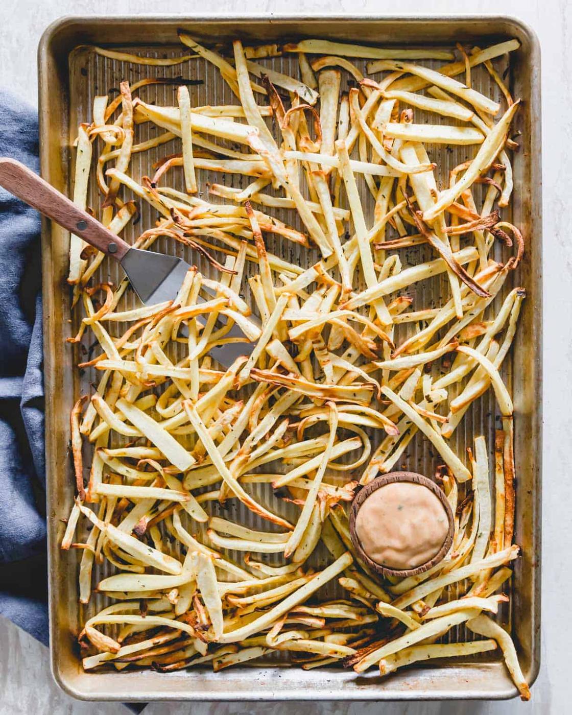 Crispy baked parsnip fries on a baking sheet with a fry sauce for dipping.