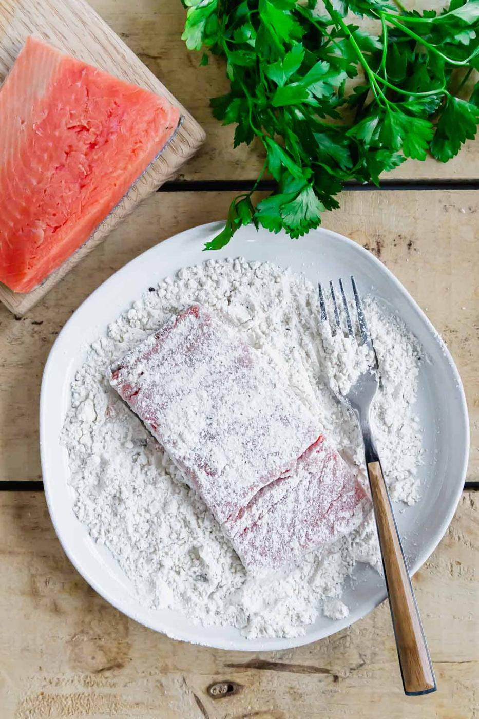 Dredging salmon in flour on a plate.