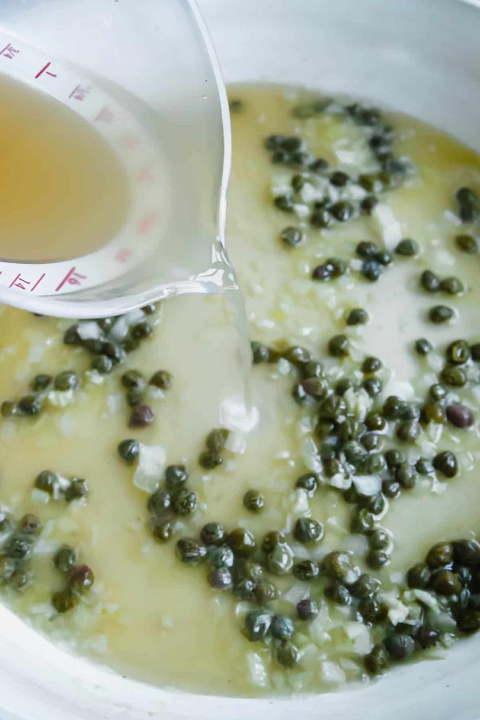Pouring broth into a skillet with shallots and capers.
