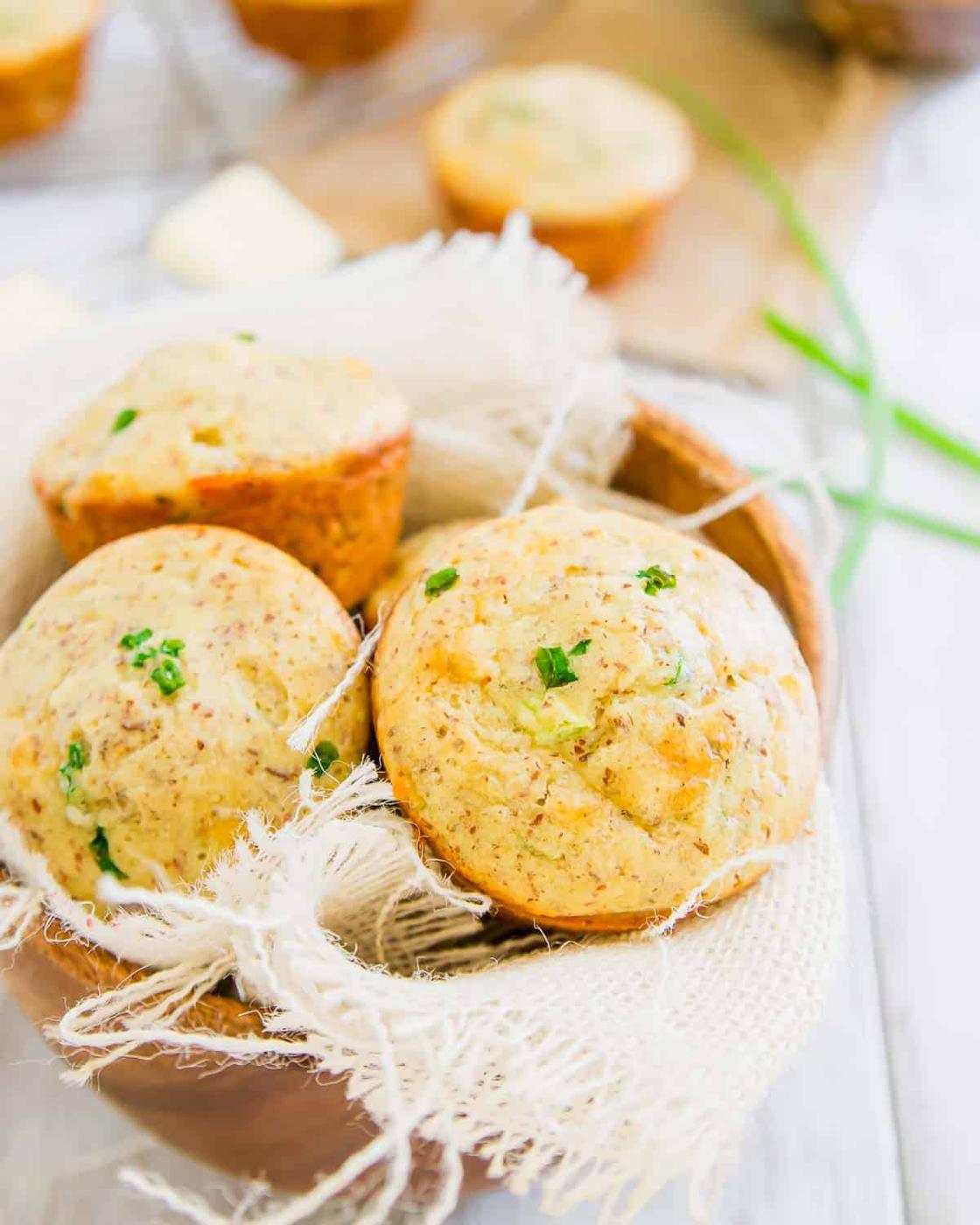 A wooden bowl lined with cloth holds three herb sausage muffins. More muffins and butter are visible in the background.