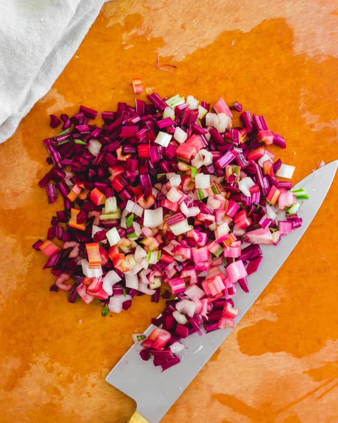 Chopped stems from beet greens and rainbow Swiss chard on a cutting board with a knife.