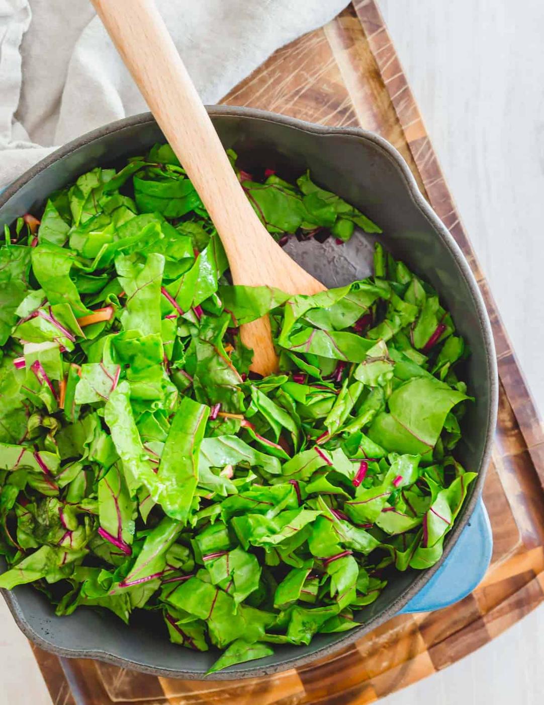 Beet greens and Swiss chard greens in a pot with olive oil and garlic and wooden spoon.