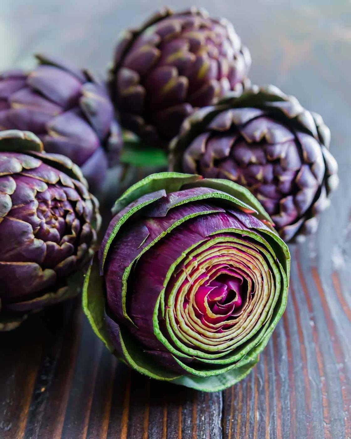 Purple artichokes on a wooden table.