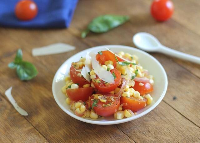 Corn and tomato salad in a small white bowl topped with parmesan cheese.