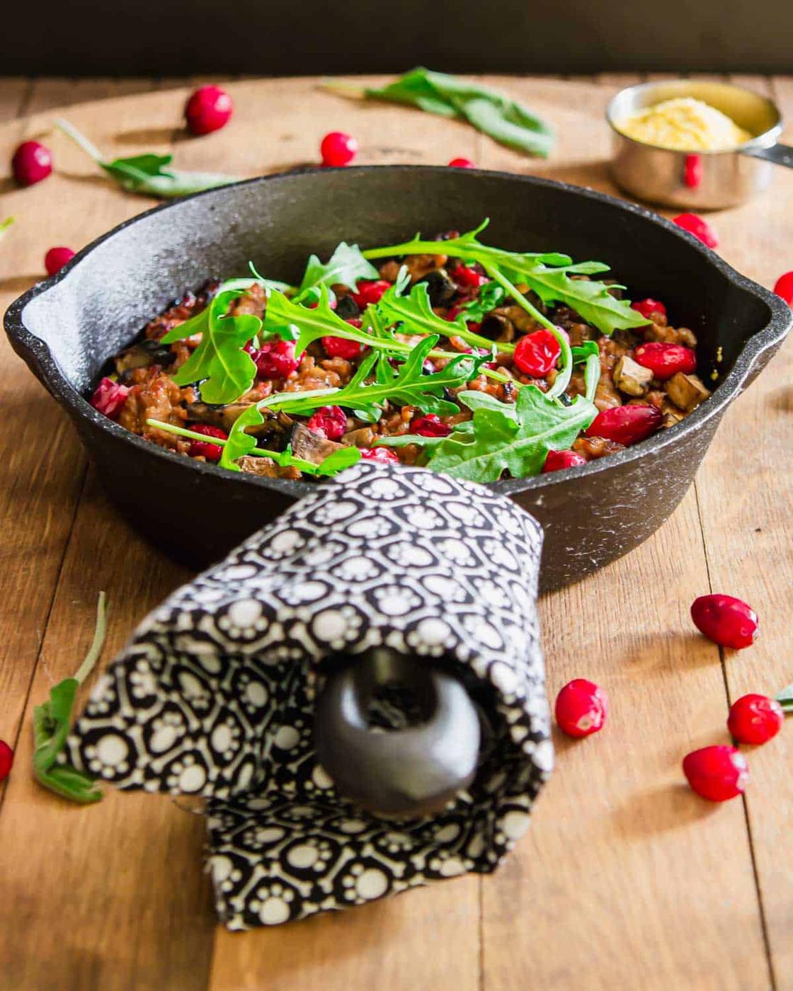 Polenta with sausage in a cast iron skillet with a black and white towel wrapped around the handle.