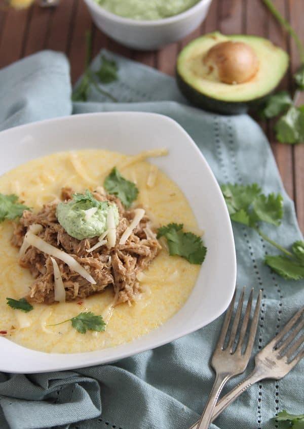 This slow cooker balsamic pulled pork is sweet and juicy served over cheesy polenta and topped with a cilantro infused avocado crema.