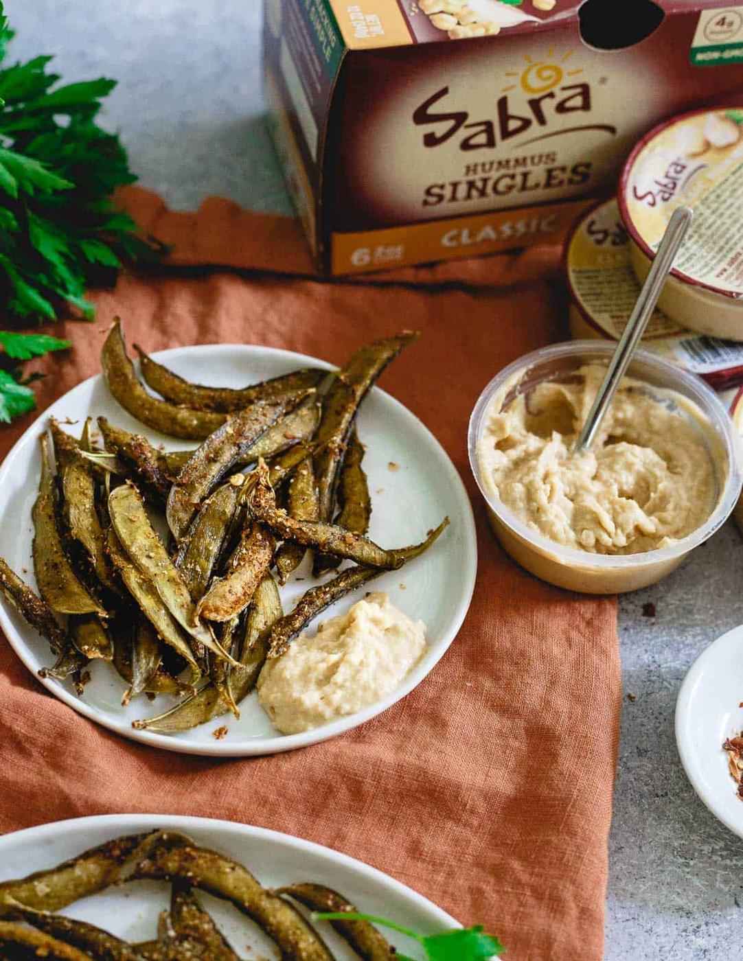 Snap pea chips on a plate with hummus as a dip.