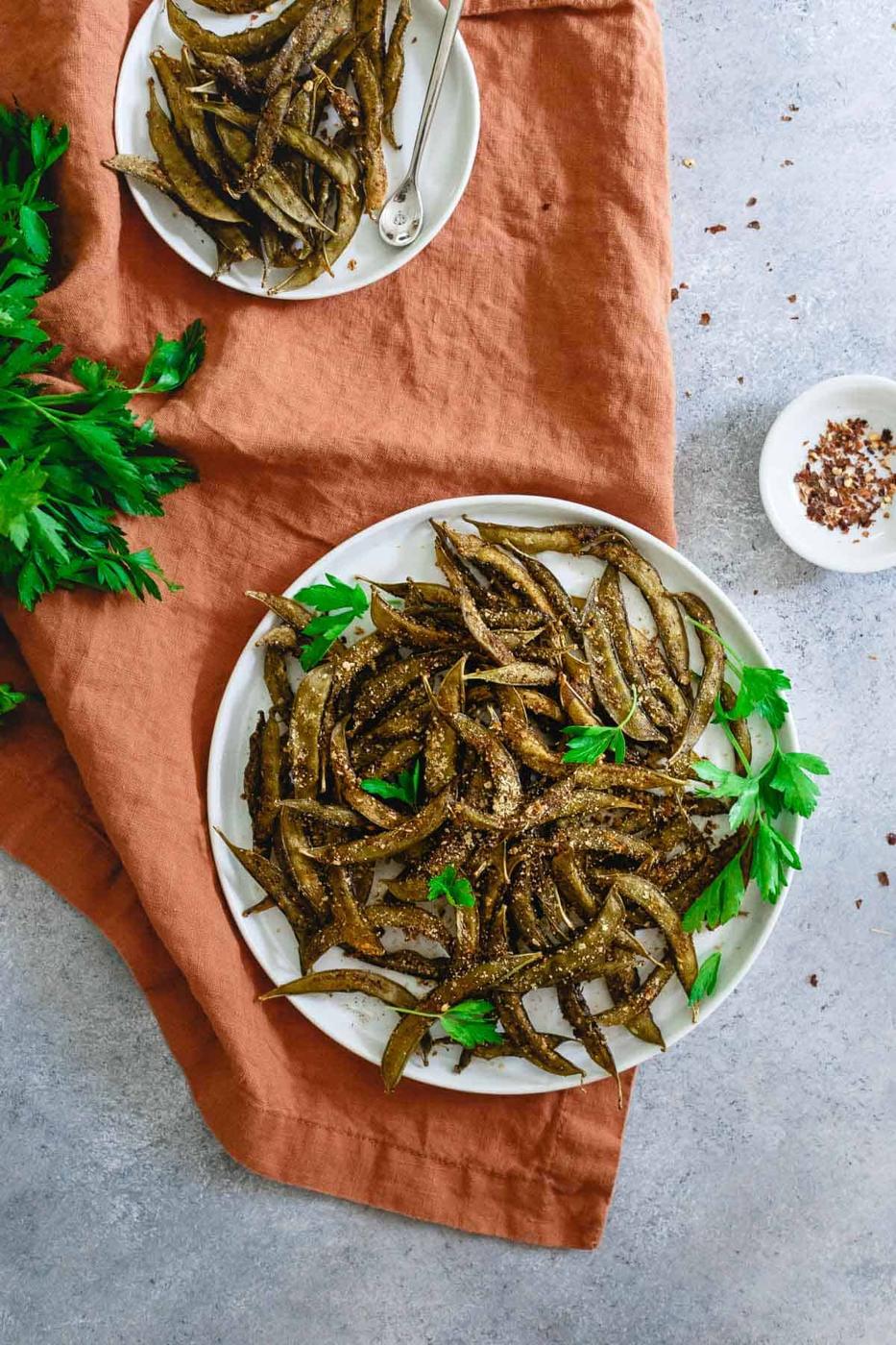Seasoned homemade snap pea chips on a white plate.