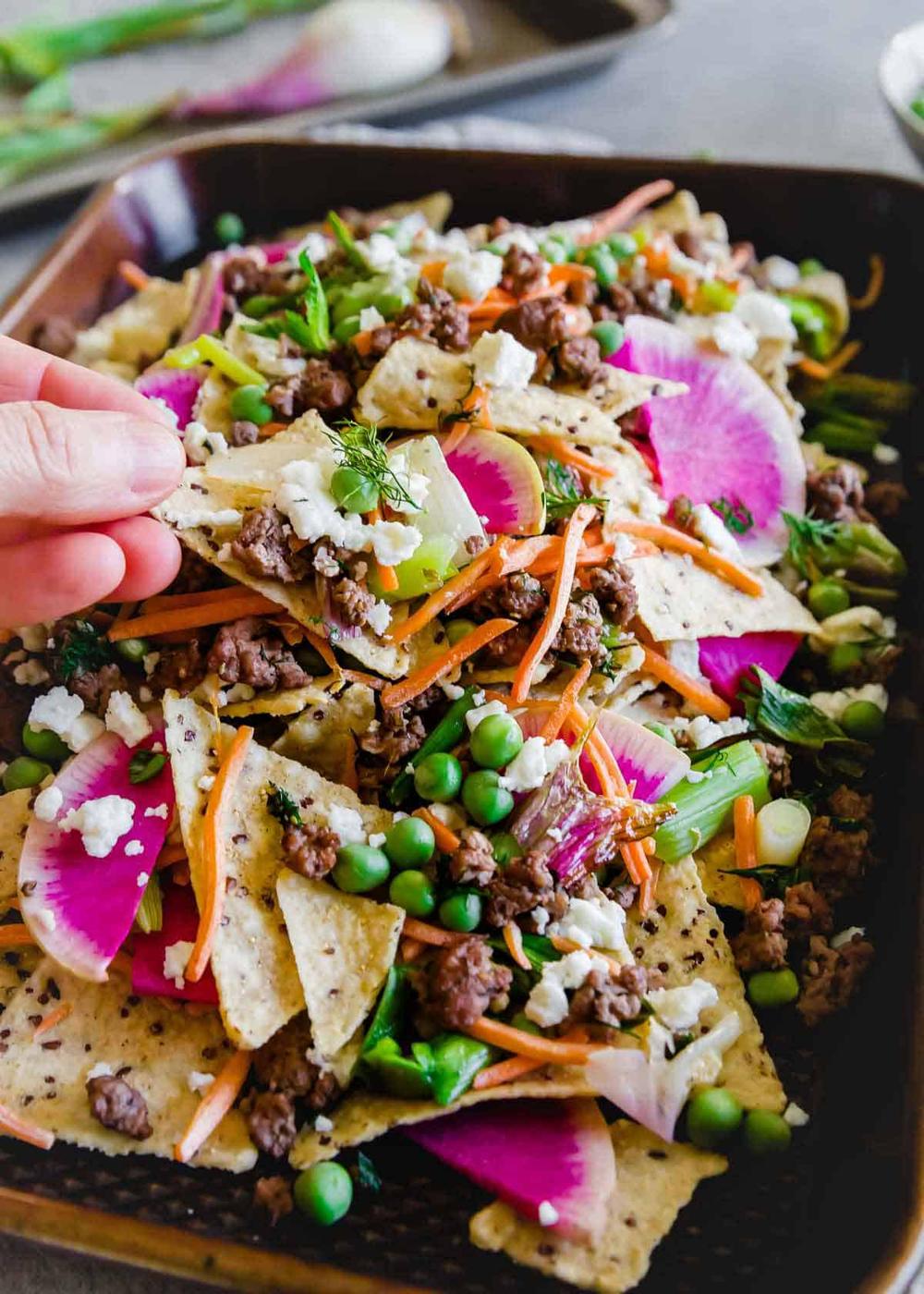 A fun spring spin on traditional nachos, these nachos use ground lamb seasoned with dill and oregano and lots of fresh spring vegetables.