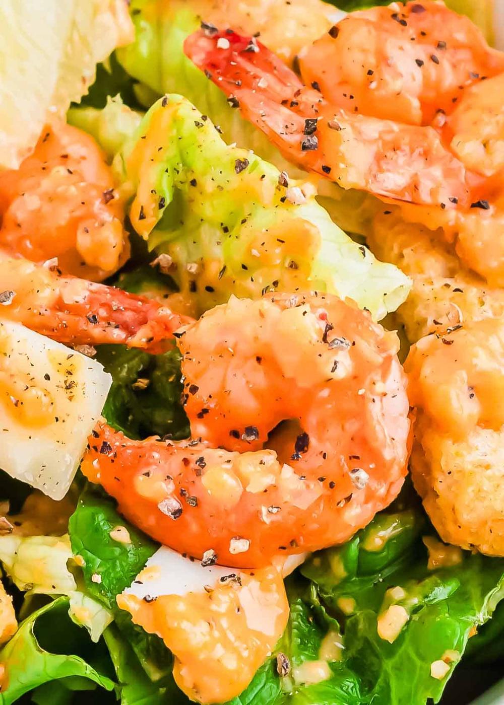 Close-up of a fresh shrimp salad with leafy greens, creamy dressing, and pepper seasoning.