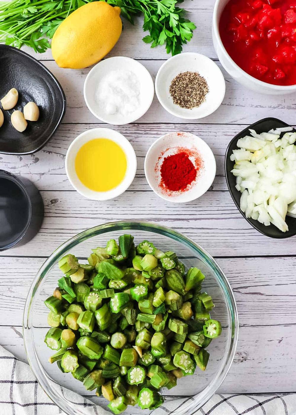 Ingredients to make okra and tomatoes on a white wooden table.