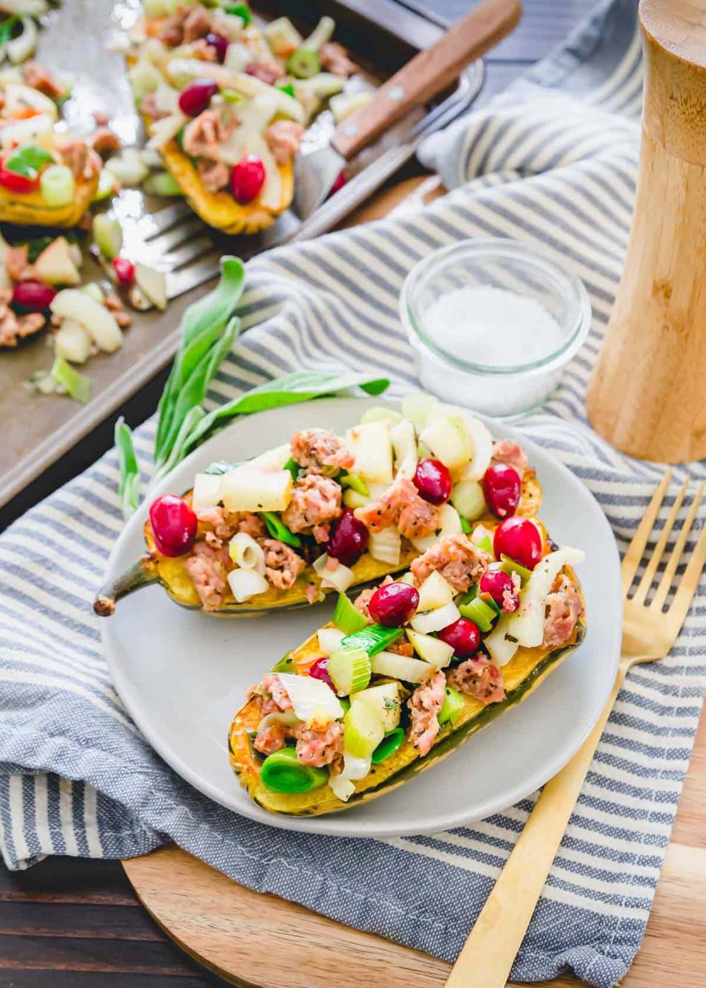 Stuffed delicata squash on a plate bursting with fall ingredients of ground pork, cranberries, fennel and leeks.