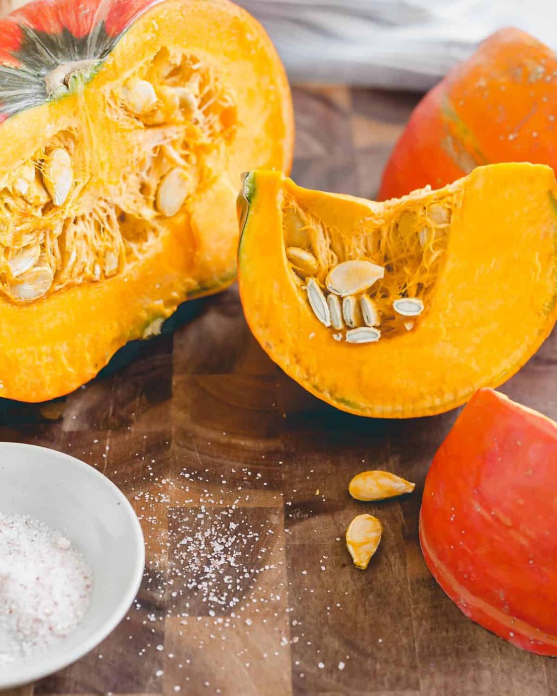Red kuri squash cut open on a cutting board with coarse salt.