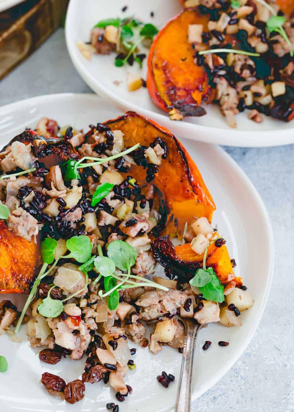 Red kuri squash served with a sausage, mushroom, apple and onion stuffing on a plate with a fork.