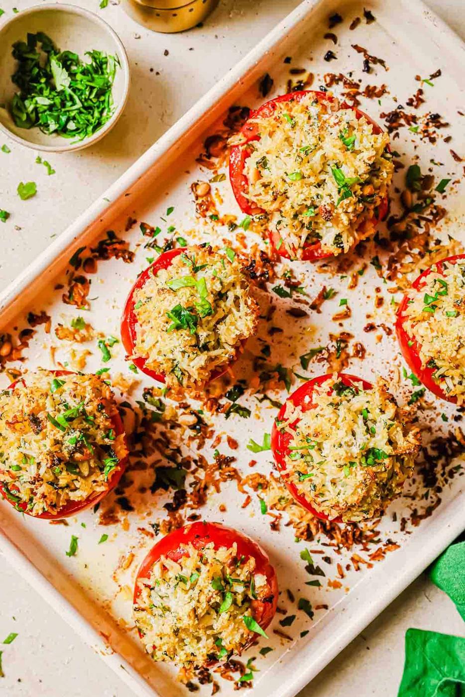 Baked stuffed tomatoes on tray topped with fresh herbs.