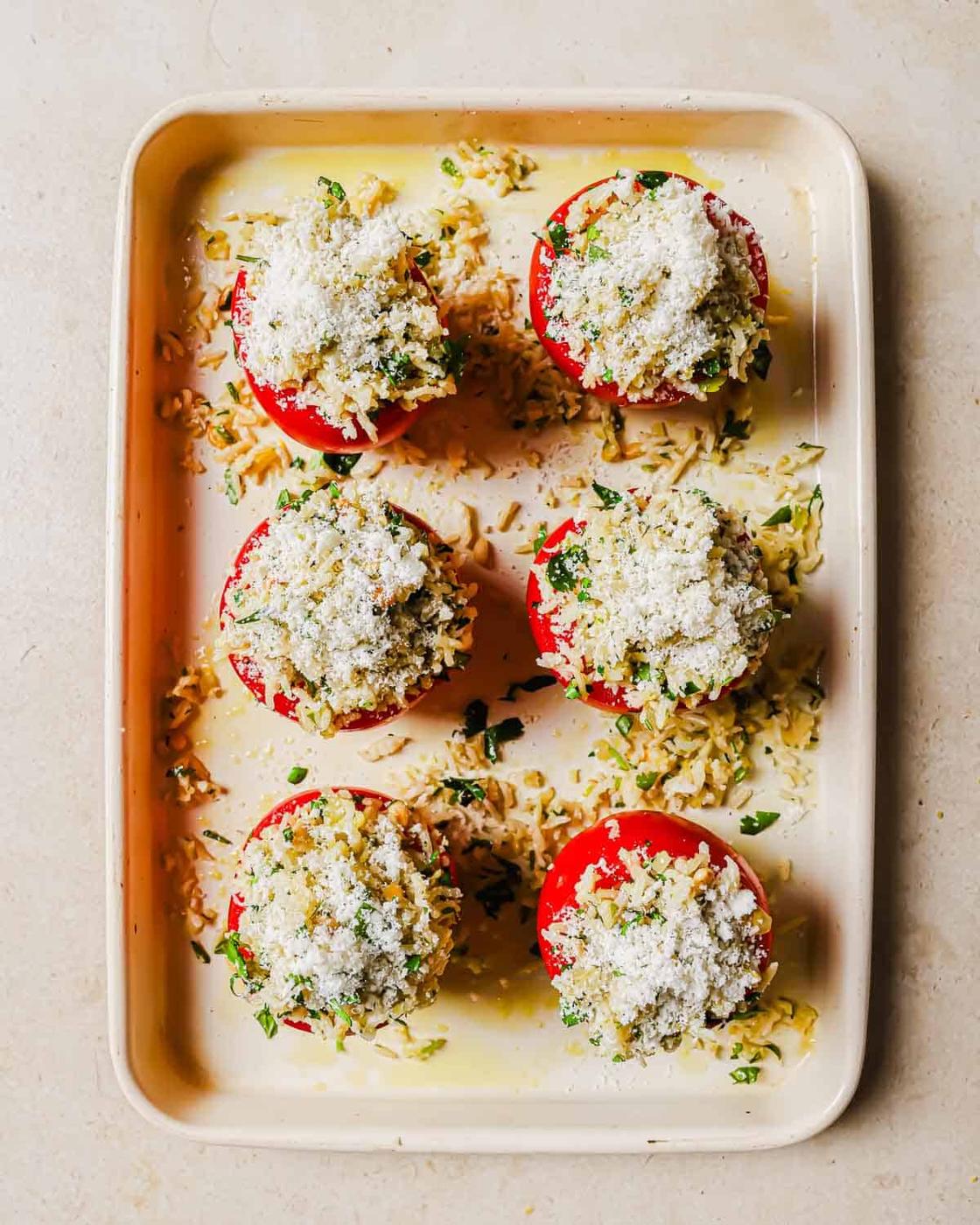 Six stuffed tomatoes filled with a mixture of rice, herbs, and topped with grated cheese, arranged in a baking tray.
