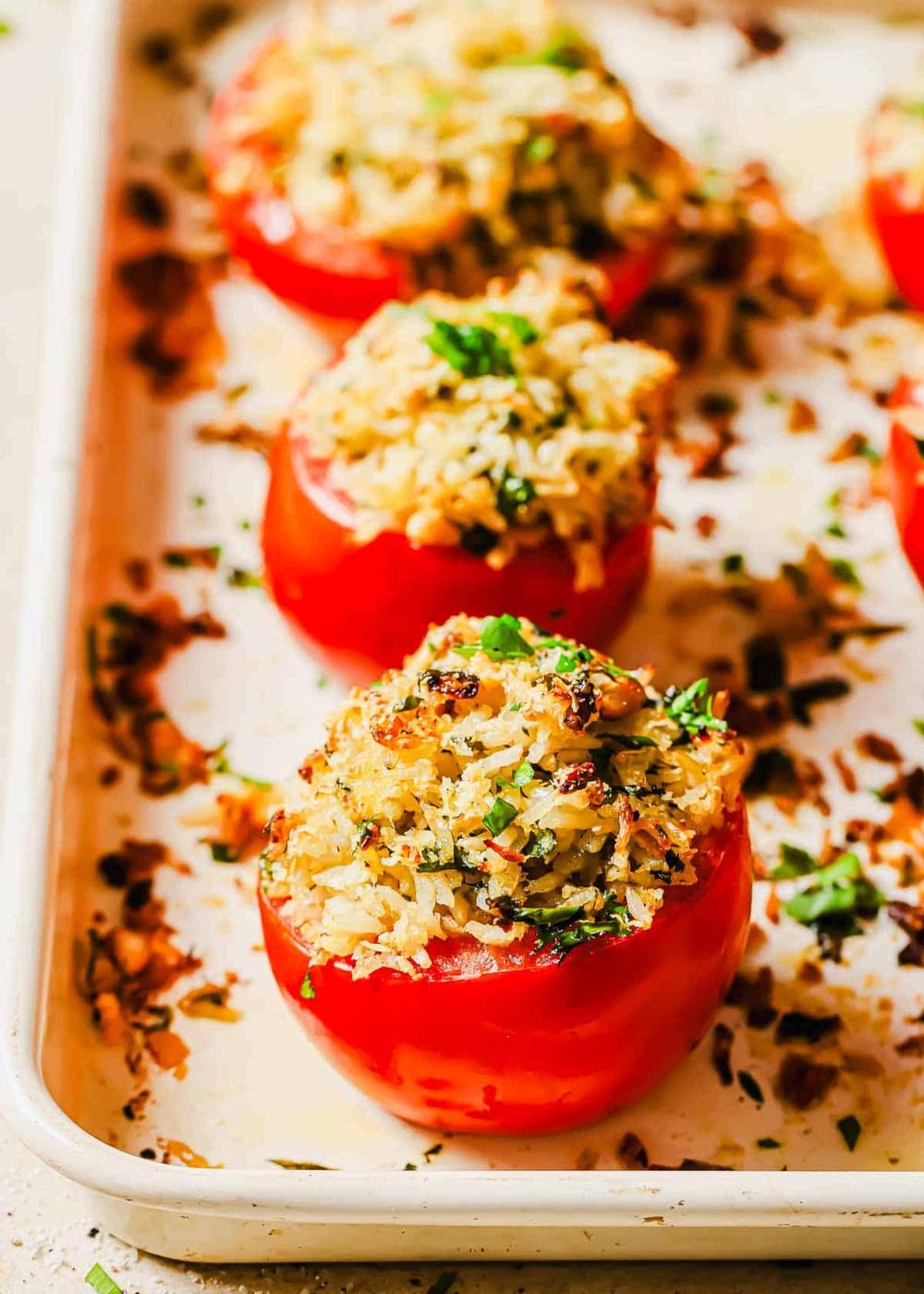 Four stuffed tomatoes with a rice and herb mixture, baked to a golden-brown color, served on a baking sheet.