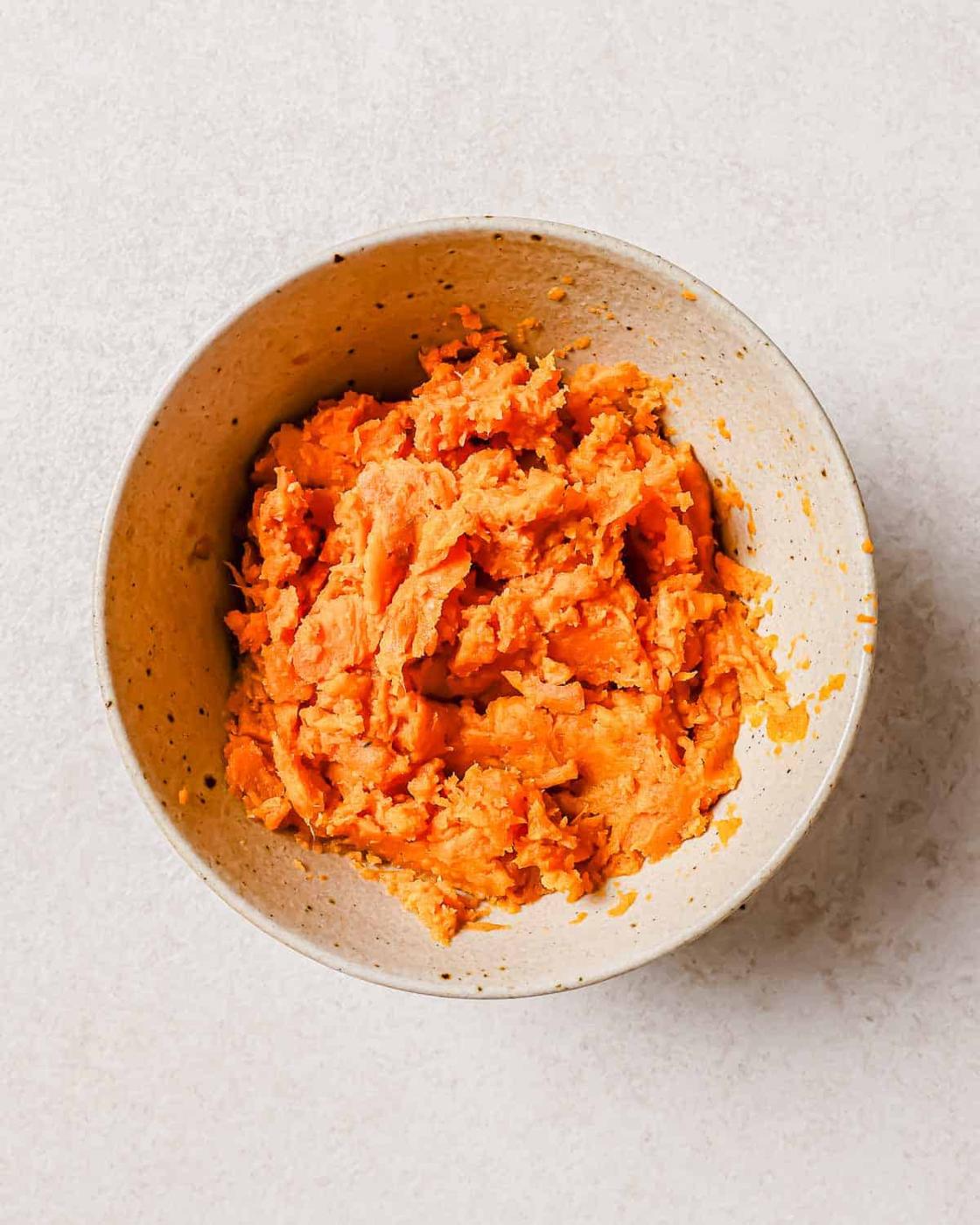 A bowl filled with mashed sweet potatoes on a white surface.