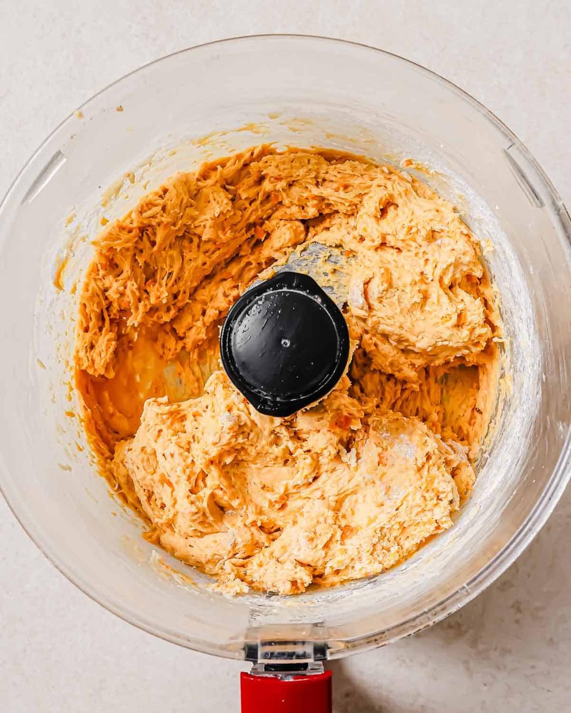 A food processor bowl filled with a thick mixture of sweet potato biscuit dough.