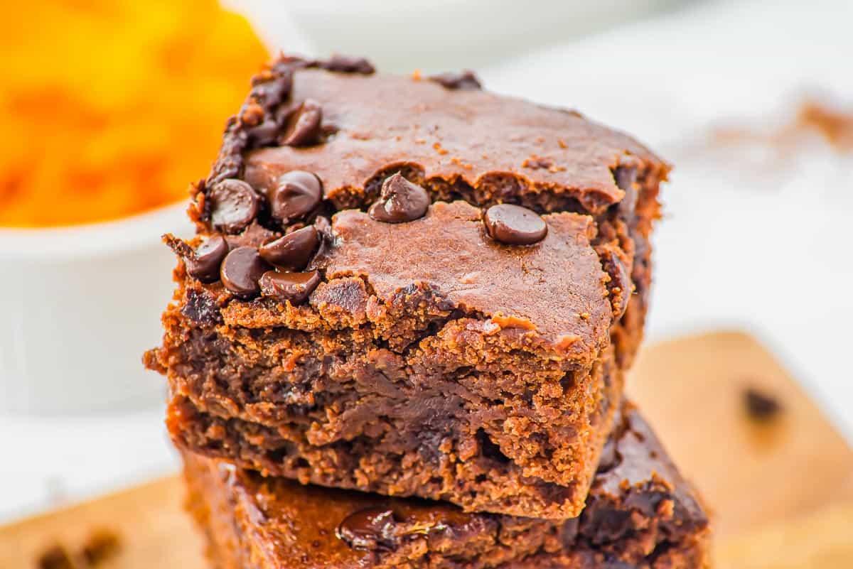 A close-up of two fudgy, chocolate chip sweet potato brownies stacked on top of each other, showing a moist, rich texture and scattered chocolate chips on top.