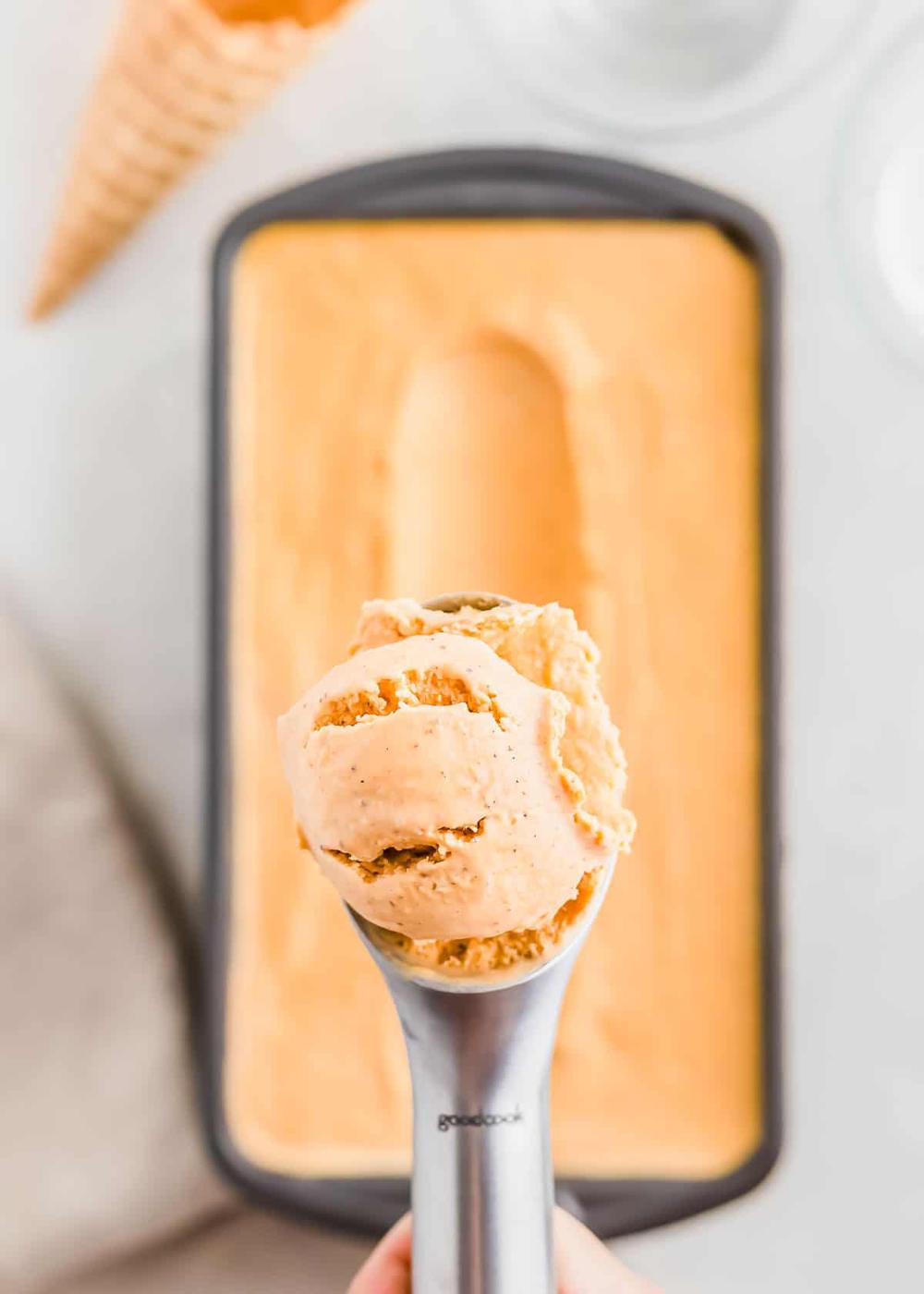 A scoop of sweet potato ice cream from a rectangular container, with an empty waffle cone placed nearby.