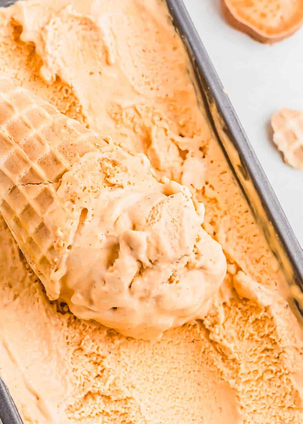 Close-up of a waffle cone being placed into a container filled with creamy sweet potato ice cream.