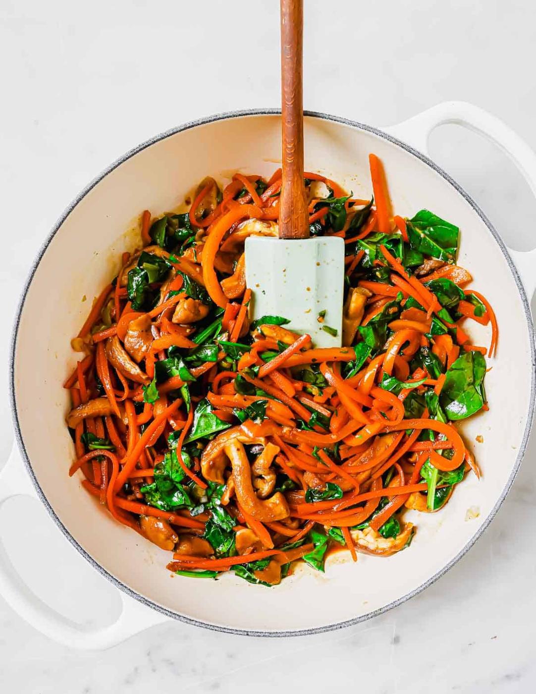 Peppers, mushrooms and spinach in a skillet with a spatula.
