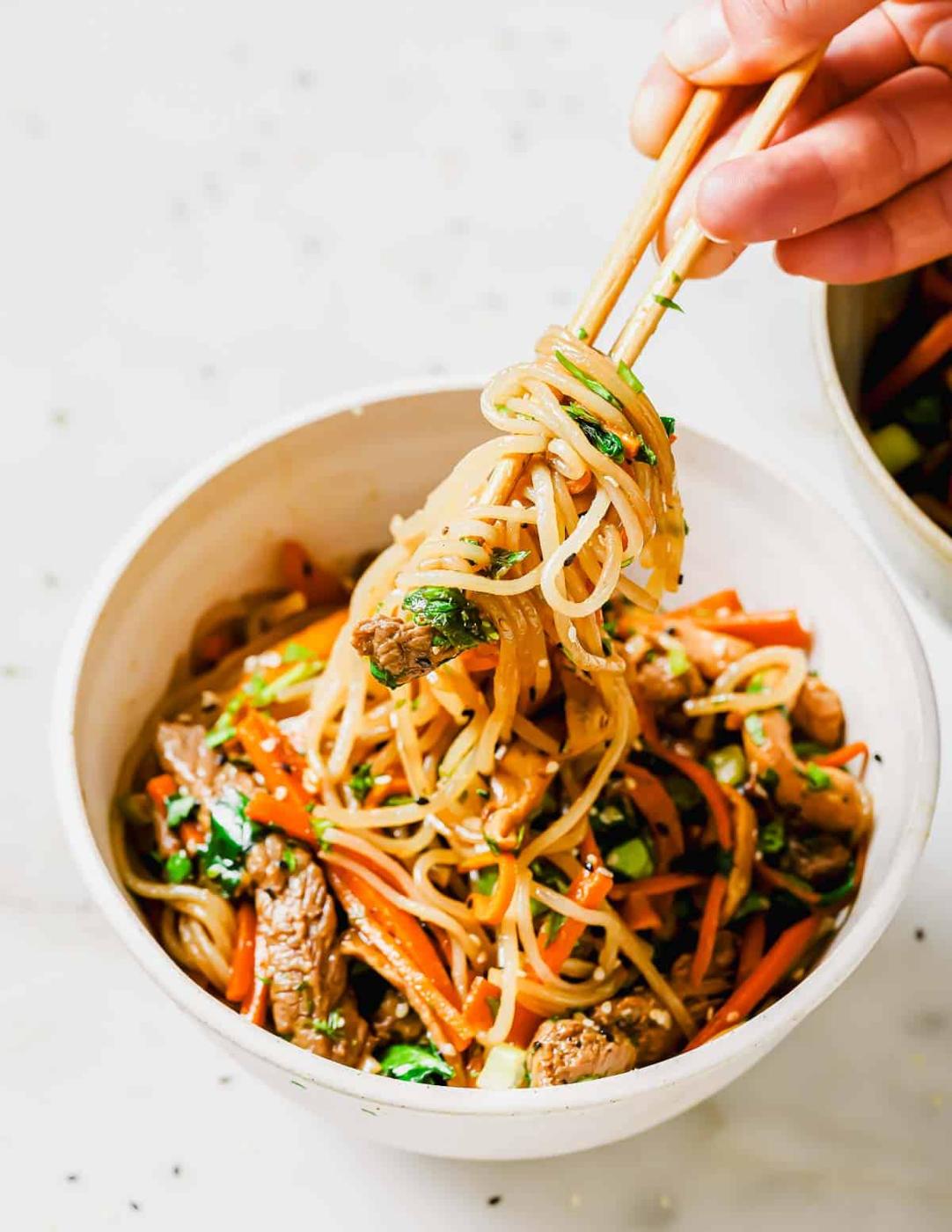 A person holding chopsticks over a bowl of sweet potato noodles.