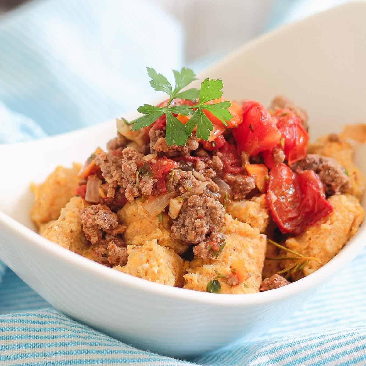 White bowl filled with a dish featuring bolognese meat sauce and sweet potato gnocchi.