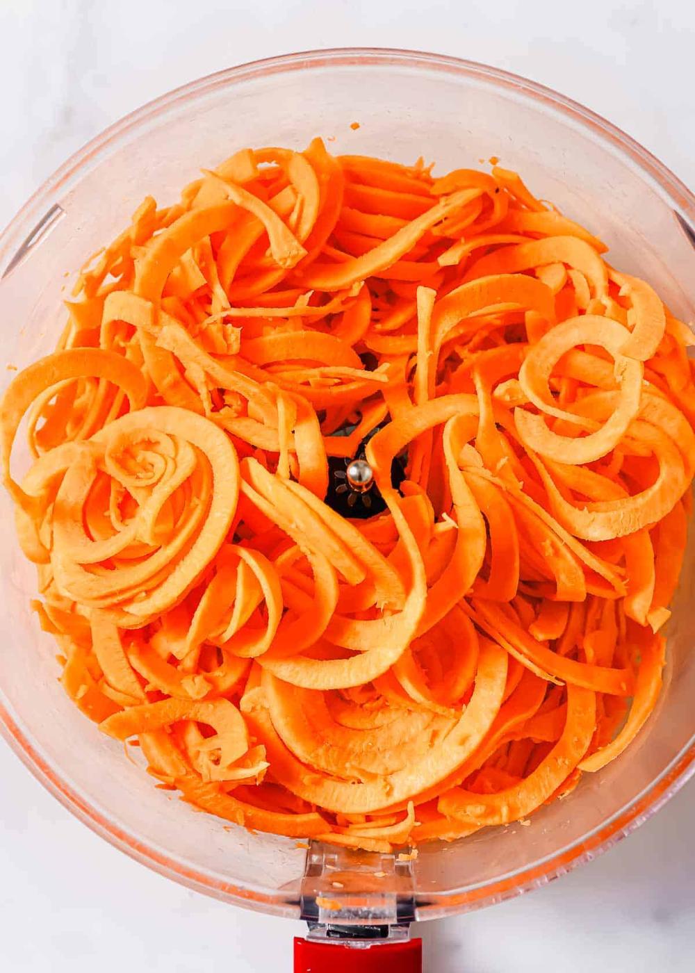 A food processor bowl filled with spiralized sweet potato noodles.