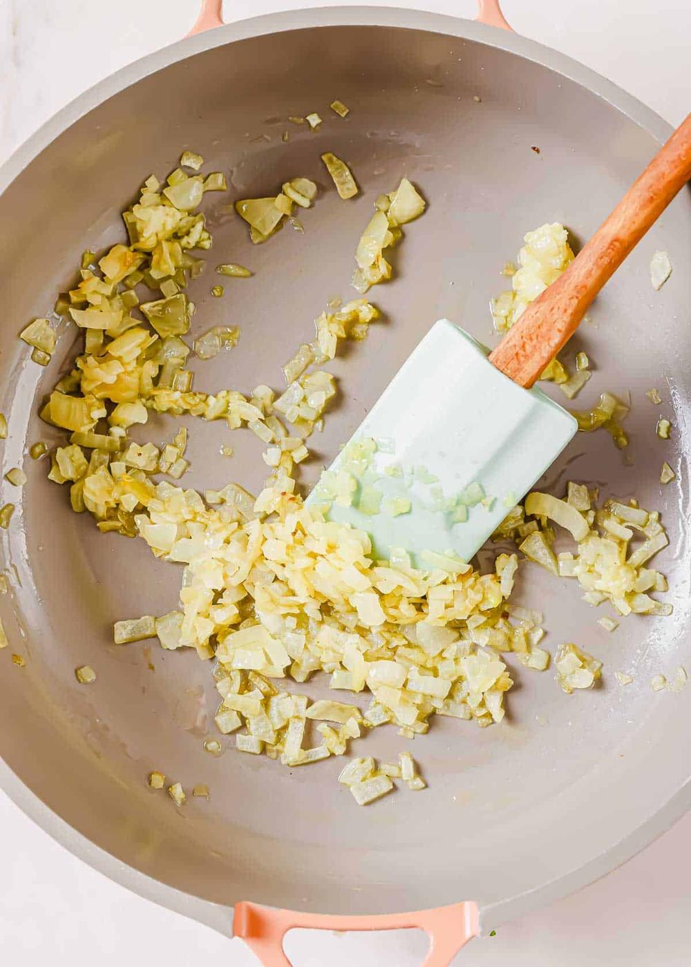 Diced onions being sautéed in a frying pan with a spatula.