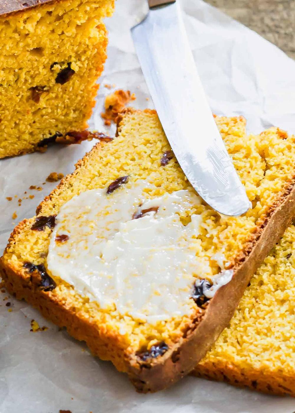 A knife spreading butter on a piece of sweet potato raisin bread.
