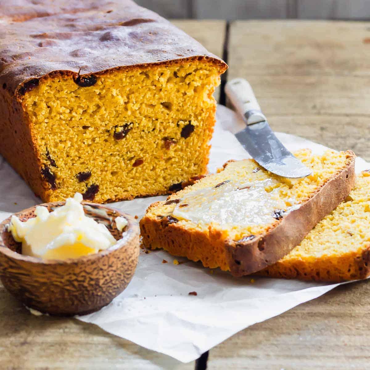 Head on shot of a loaf of sweet potato bread with butter in a bowl and two slices on parchment paper and a knife.
