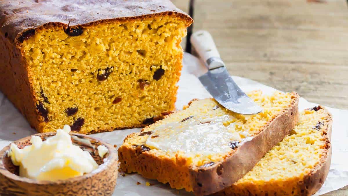 A loaf of sliced sweet potato raisin bread with buttered slices on parchment paper.