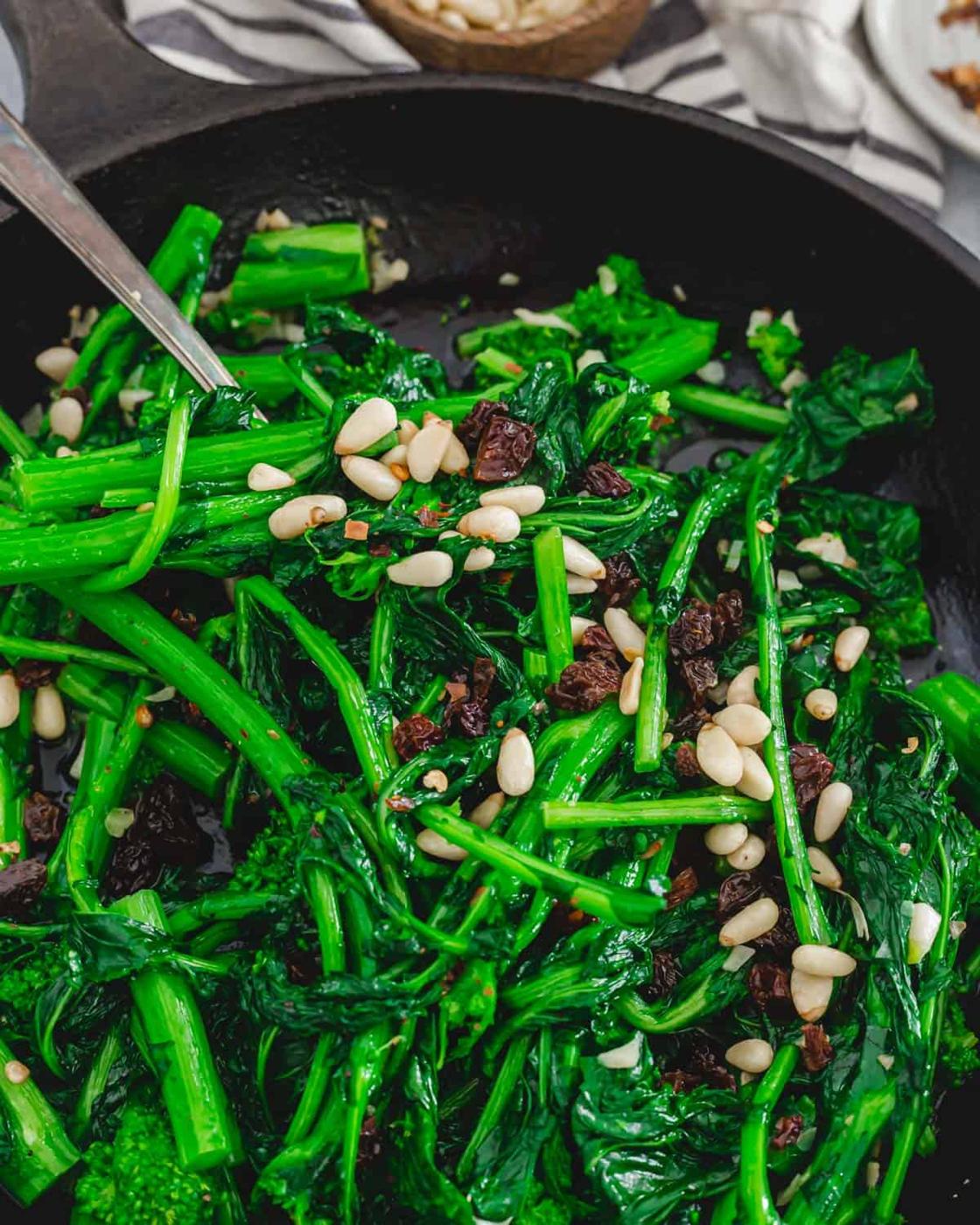 Broccoli rabe side dish recipe with toasted pine nuts and dried cherries and raisins in a skillet.