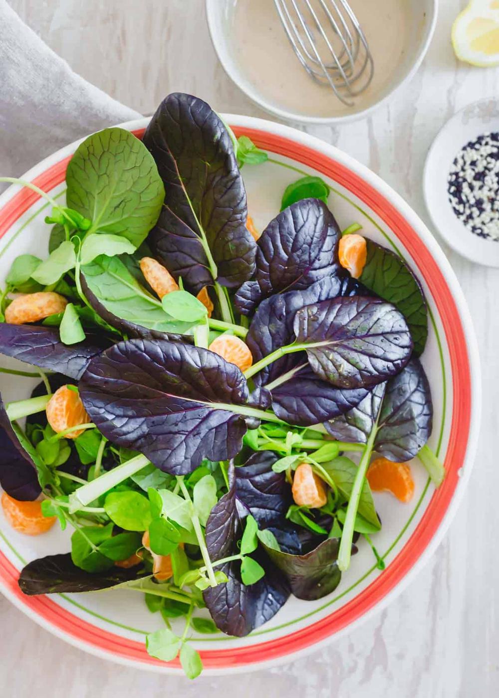 Freshly washed tatsoi greens, pea shoots and clementines in a serving bowl.