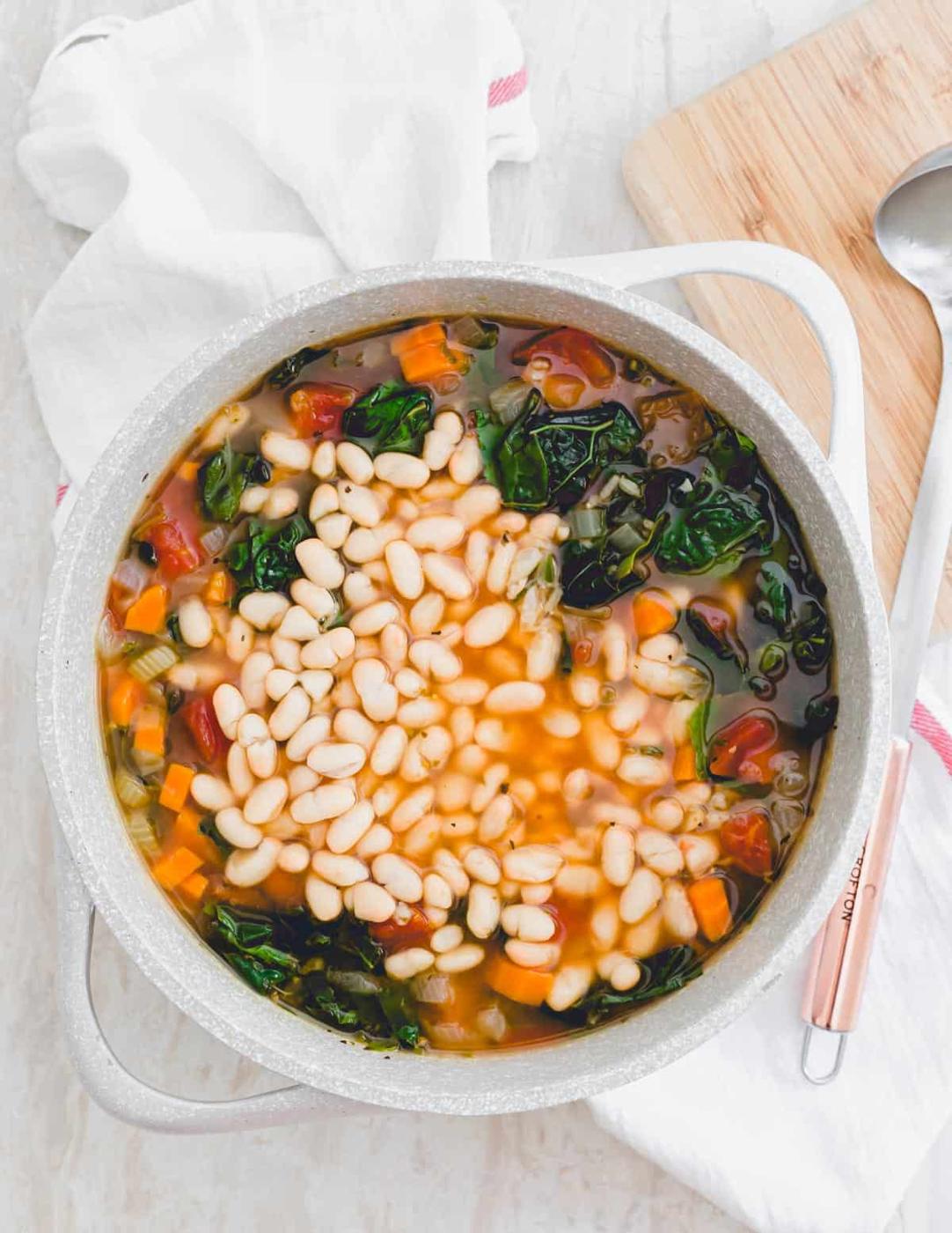 A pot of Tuscan kale soup with added white beans and ladle on the side.