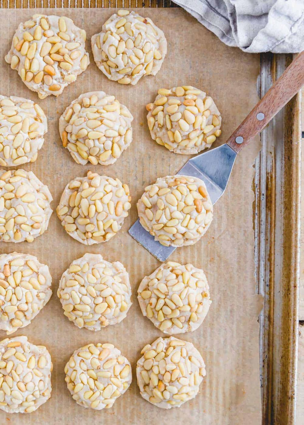 Baked vegan pignoli cookie recipe on a sheet pan with a spatula.
