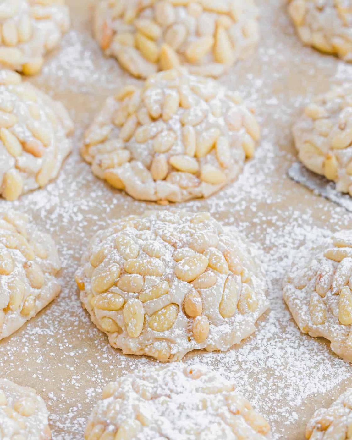 Pignoli cookies on a baking sheet dusted with powdered sugar.