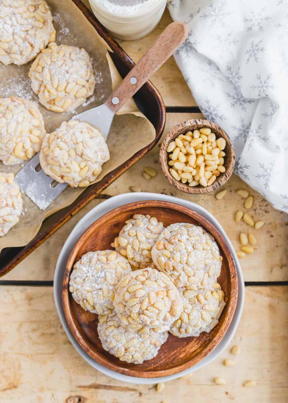 Italian pine nut cookies made without egg whites on a plate with pine nuts scattered about.