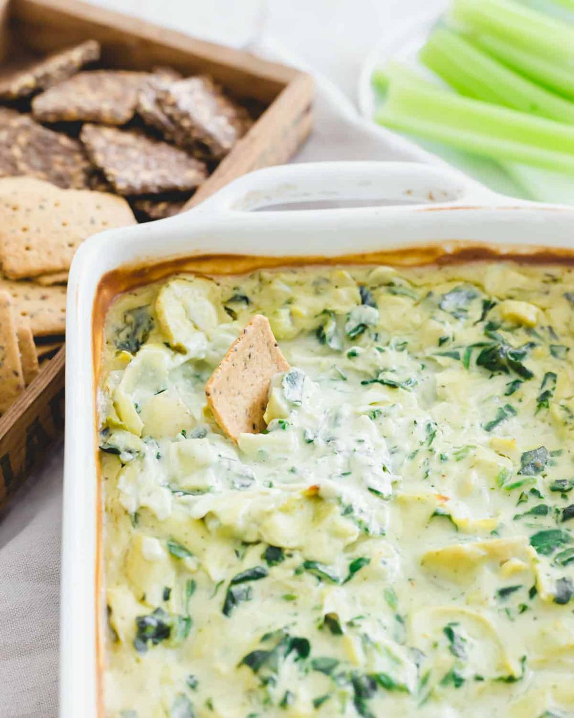 Cracker dipped in creamy vegan spinach artichoke dip.