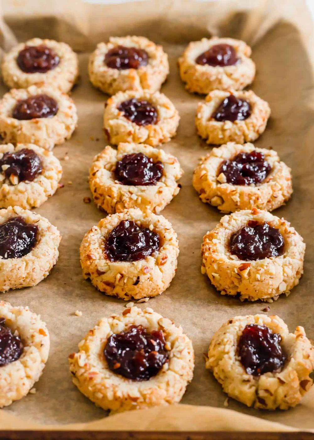 Baked almond flour thumbprint cookies with raspberry jam on a baking sheet.