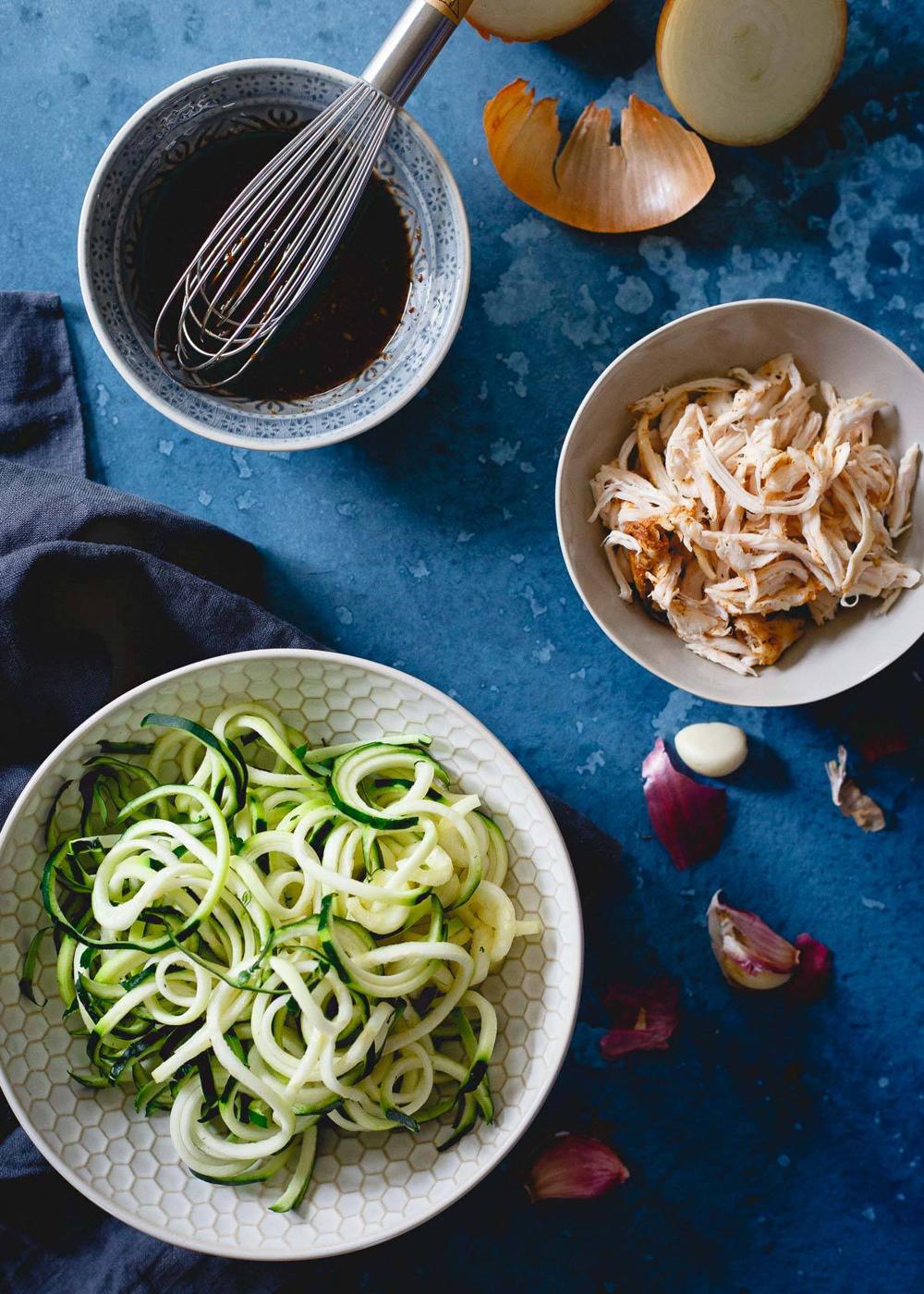 Zucchini noodles in a bowl with shredded chicken and sauce.