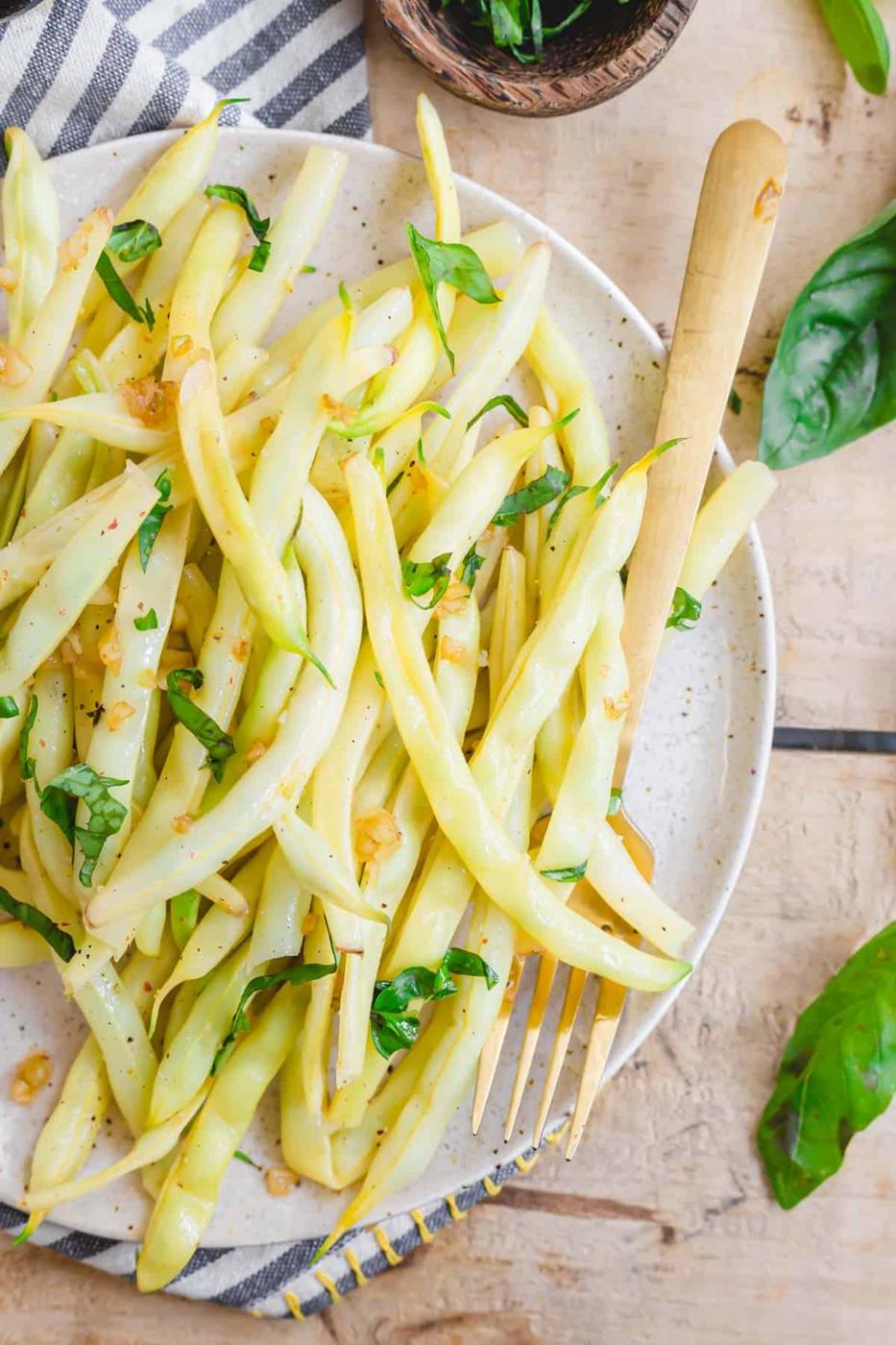 Wax bean recipe with garlic and basil on a ceramic plate with a serving fork.