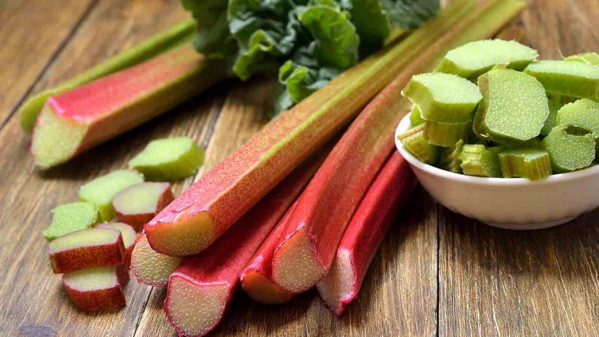 Fresh rhubarb stalks next to sliced rhubarb pieces on a wooden surface.