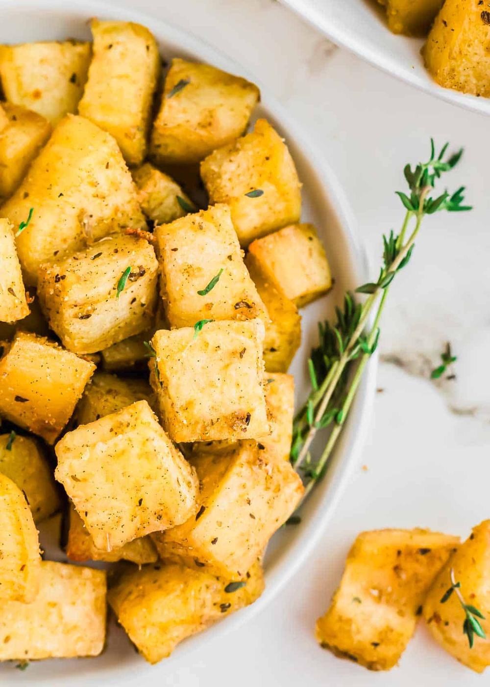 A close-up of a bowl filled with seasoned, roasted white sweet potato cubes garnished with sprigs of fresh thyme.