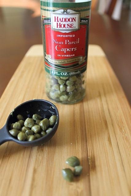 Capers being measured out in a spoon for quinoa cakes.