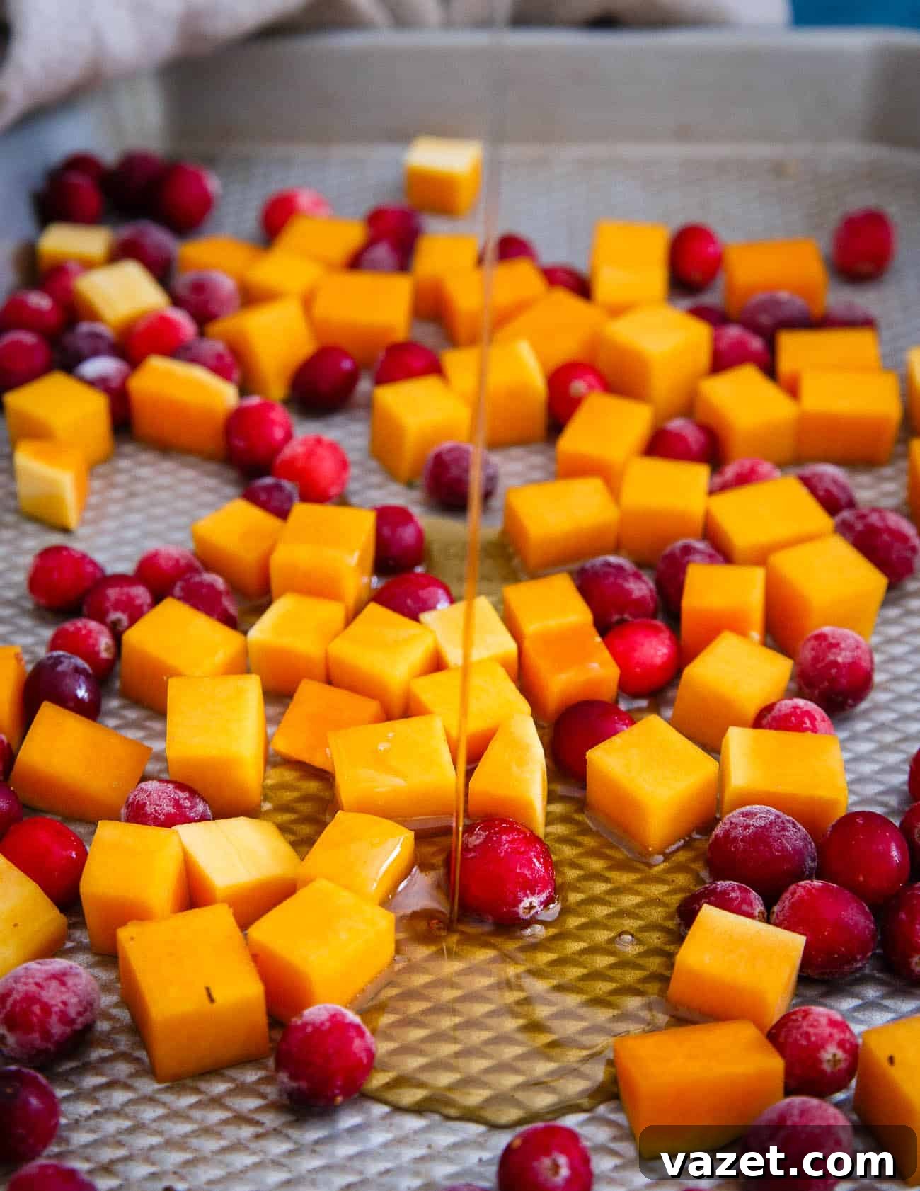 Butternut squash and fresh cranberries coated in maple syrup, spread on a baking sheet, ready for roasting.